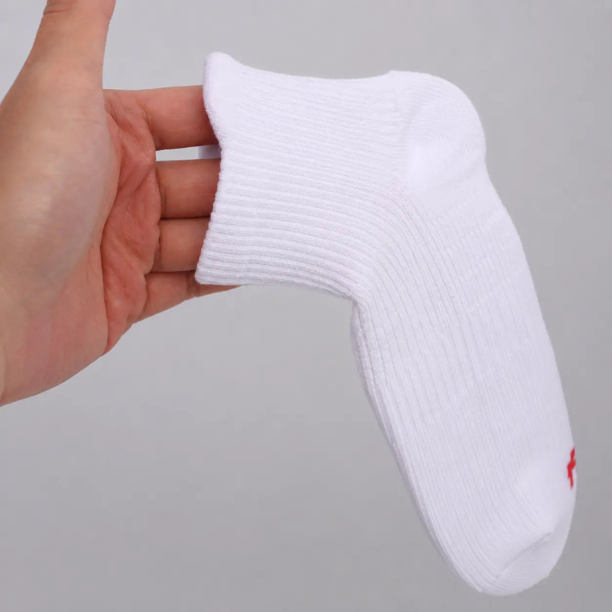 White ankle compression sock held by hand to show its ribbed fabric and ankle-height shape
