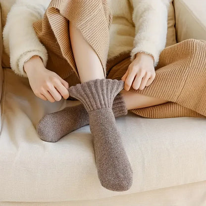 Woman pulling on a taupe cashmere wool sock while sitting comfortably on a sofa