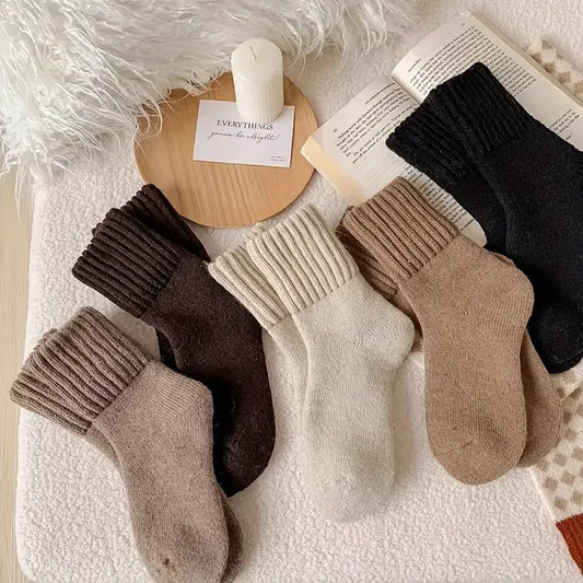 Five pairs of thick cashmere wool socks in black, brown, cream and beige arranged beside an open book