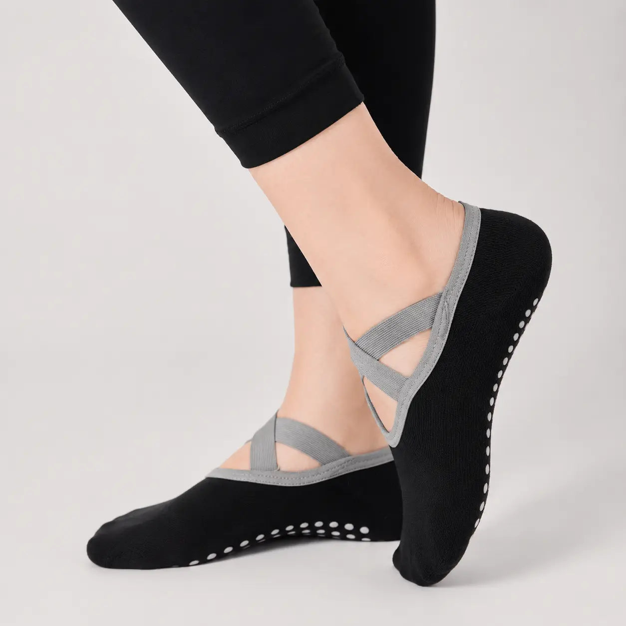 Black Pilates grip socks worn with grey crossover straps and low-cut studio fit