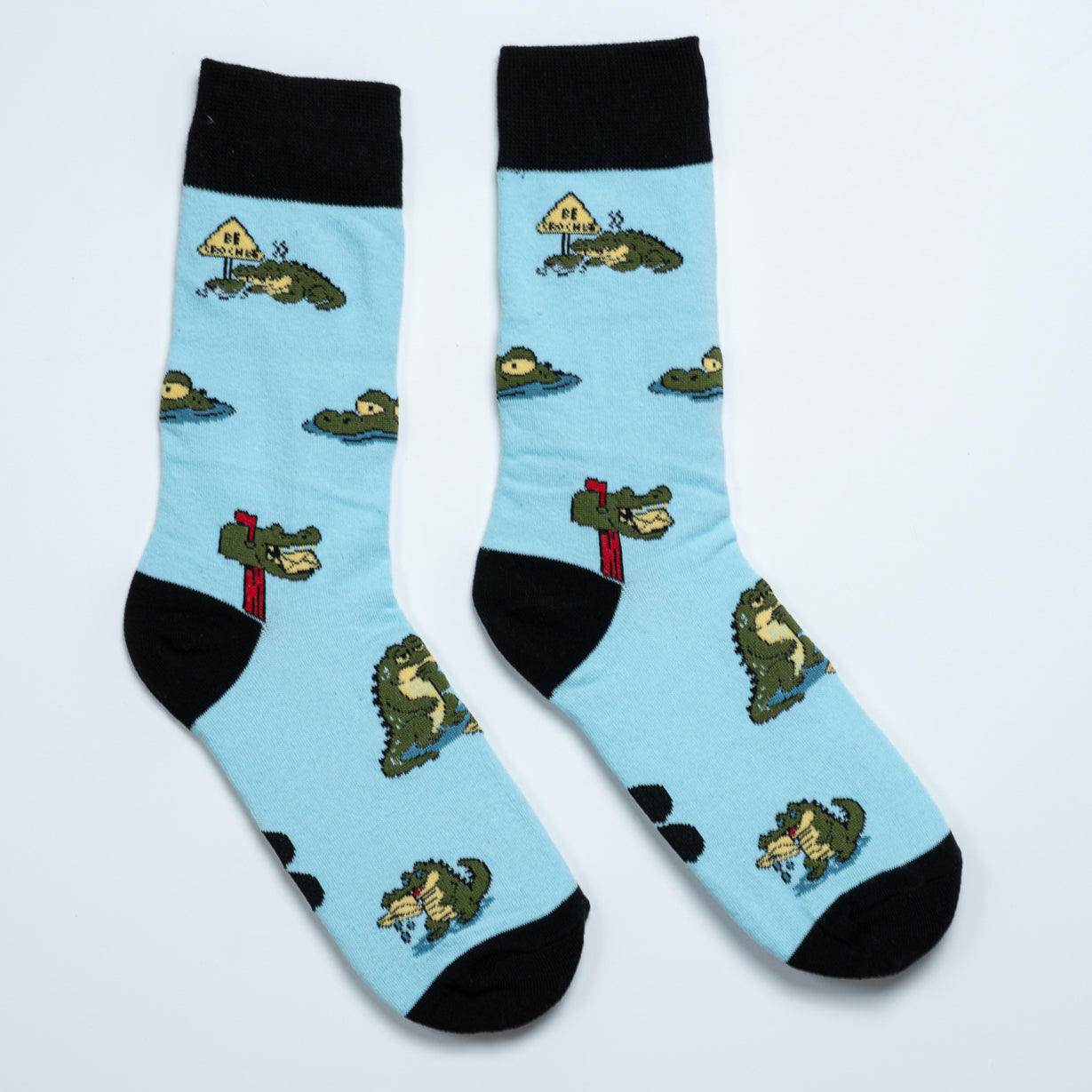 Light blue crocodile crew socks with black cuffs, heels and toes featuring playful croc scenes