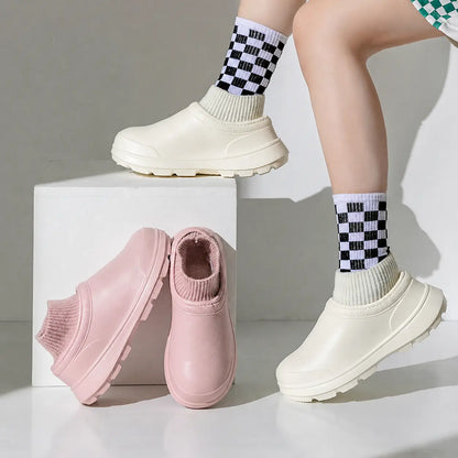 Woman wearing white SmileyClox clogs beside a pair of pink slip-on clogs
