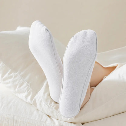 White BareLite footie socks shown from the soles while worn with light trousers