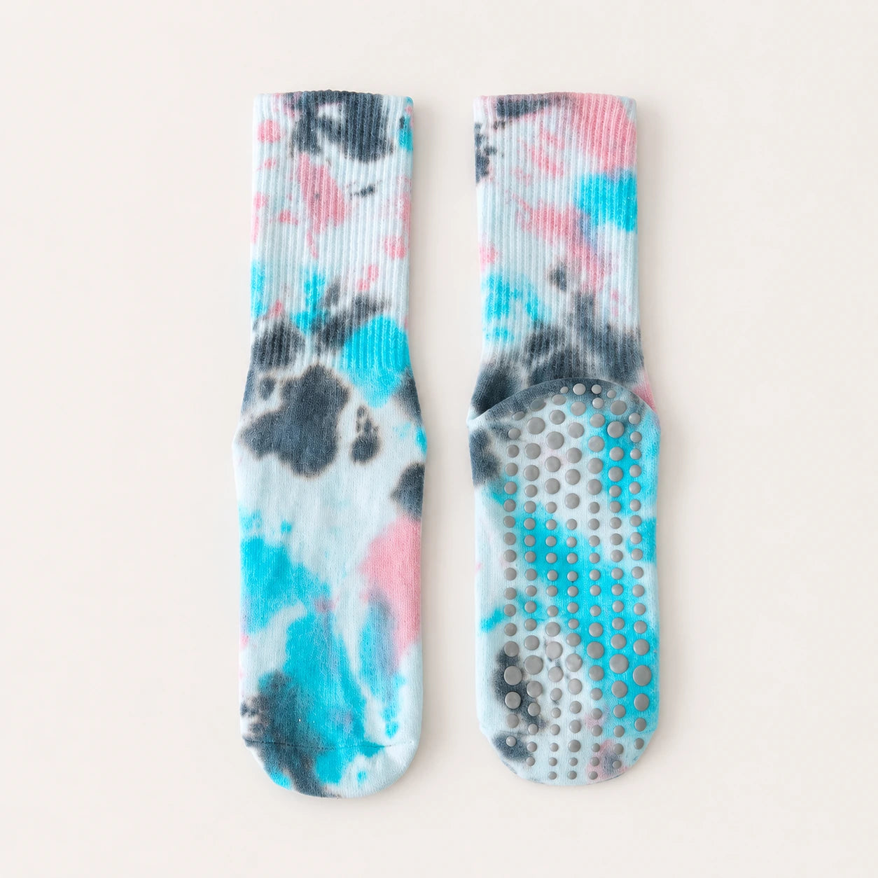 A pair of ribbed grip socks with a tie-dye pattern in turquoise, pink, and charcoal gray on a white base, displayed flat against a light beige background.