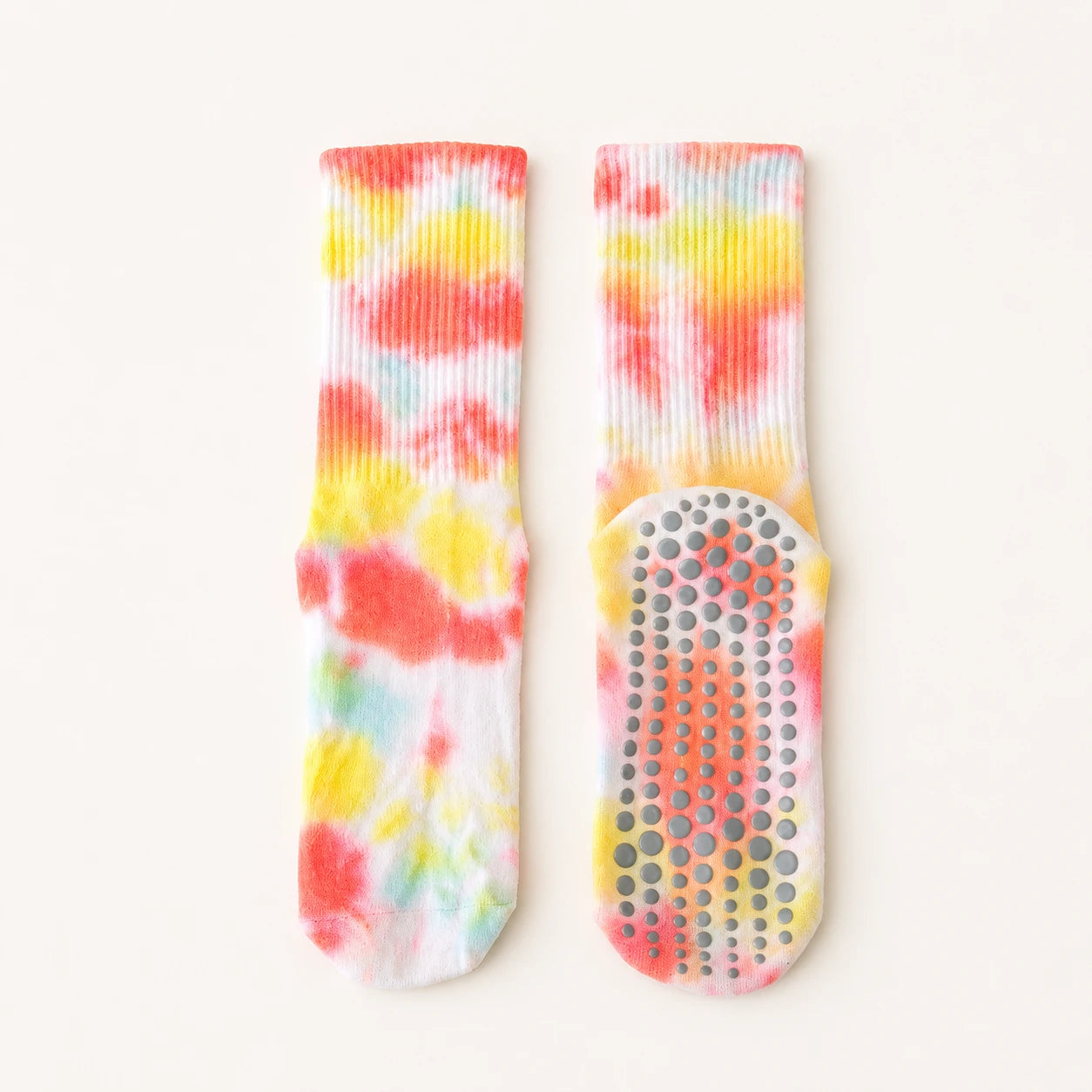 A pair of white ribbed socks with a vibrant tie-dye pattern in red, orange, yellow, and light blue, featuring a gray non-slip grip sole.