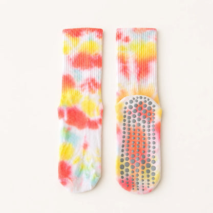 A pair of white ribbed socks with a vibrant tie-dye pattern in red, orange, yellow, and light blue, featuring a gray non-slip grip sole.