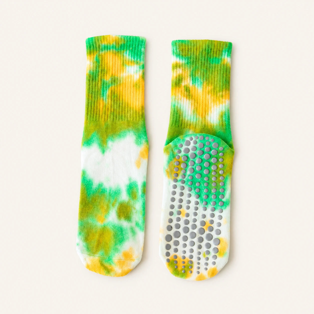 A pair of tie-dye grip socks shown flat on a light cream background. One sock is oriented vertically to show the ribbed knit cuff and toe, while the other is horizontal to display the textured non-slip grip sole.