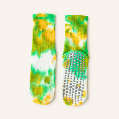 A pair of tie-dye grip socks shown flat on a light cream background. One sock is oriented vertically to show the ribbed knit cuff and toe, while the other is horizontal to display the textured non-slip grip sole.