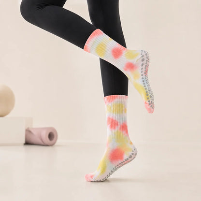 A person wearing black leggings and colorful tie-dye grip socks with gray non-slip pads, shown against a clean light beige studio background.