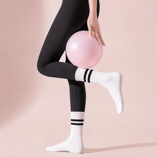 Woman wearing white Studio Crew Grip Socks with black stripes while holding a pink Pilates ball
